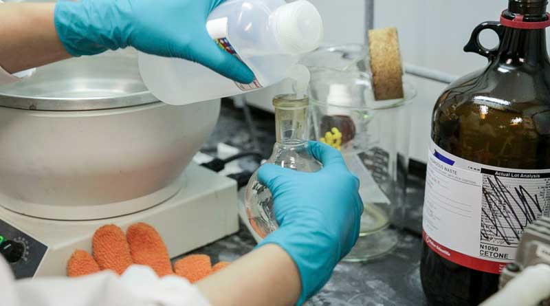 close up of hands in blue gloves pouring a liquid into a test tube