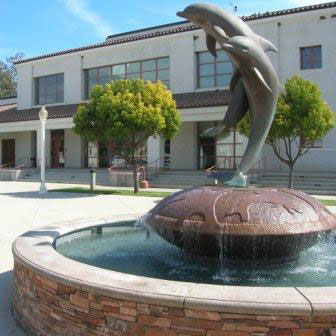Fountain with a statue of two dolphins in the center with a lecture hall building in the background